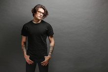 Hipster Handsome Male Model With Glasses Wearing Black Blank T-shirt And Black Jeans With Space For Your Logo Or Design In Casual Urban Style