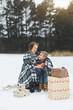 © sofiko14 - Mother and baby sitting on wooden sledge in winter forest and drinking hot tea. Christmas gifts presents on the snow. Winter snowy forest on the background. Christmas vacation.