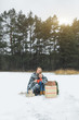 © sofiko14 - Mom and son spending time together at winter day. Mother and son covered with plaid, holding cups with hot drinks, sitting on wooden decorated sledge, outdoors, in winter snowy forest