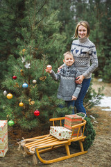 Mother and her little son decorating Christmas tree outdoors in winter forest. New Year, Christmas and family concept