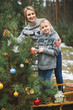 © sofiko14 - Family, young mother and little son, wearing knitted sweaters, decorating fir tree in the forest or park. Colorful decorations, wooden sledge, Christmas presents