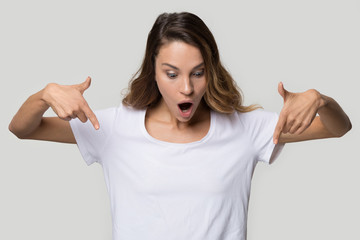 Wall Mural - Excited young woman with open mouth pointing finger down