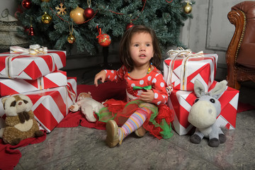 little girl in a red dress near the Christmas tree among gifts