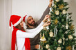 Young couple guy with girl decorate Christmas tree, celebrating traditional holiday New Year at home