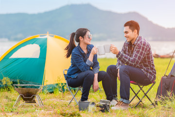 asian young couple sitting drinking coffee to happy near lake and the tent camp on outdoors camping.