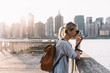 © BullRun - Side view of skilled hipster girl with instant camera clicking picture of city landscape standing at urban setting with Manhattan view, positive female tourist with backpack enjoying getaway