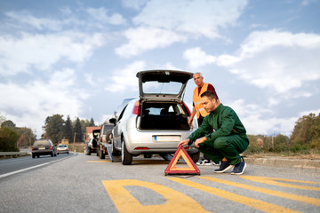 Repairer, transports a broken car on the road and placing a triangle