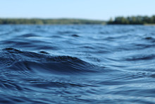 Blue Water Clear Sky Sunny Day On Finnish Lake Water Waves Close Up. Beauty Of Nature Skyline And Forest With Deep Colored Water. Photo From Boat