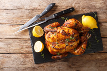 Traditional Rotisserie Chicken Served With Lemon Closeup On A Slate Board On A Table. Horizontal Top View