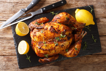 Wall Mural - Homemade chicken rotisserie with thyme, lemon closeup on a slate board. Horizontal top view