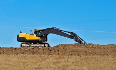  Side view of a new excavator among brown dirt and blue sky.