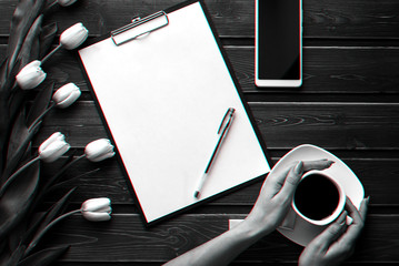 Wall Mural - White tulips on a wooden table with an empty paper tablet and smartphone and a Cup of coffee in women's hands