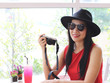 © Phuttharak - Beautiful Asian young woman wearing hat , sunglasses and red sleeveless holding camera in her hand and smiling..