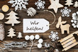 One White Label With German Text Wir Helfen Means We Help. Frame Of Christmas Decoration Like Tree, Sled, Star And Fir Cone. Wooden Background With Snowflakes