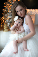 Happy mother with newborn daughter on a background of the Christmas tree. New Year. Christmas and family concept.Portrait of a happy young mother playing with her little daughter in a bright room on C