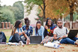© AS Photo Family - Group of five african college students spending time together on campus at university yard. Black afro friends sitting on grass and studying with laptops.