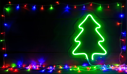 The beautiful christmas background with a lot of colorful lights and green neon christmas tree on the wooden desk