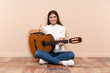 © luismolinero - Young woman with guitar sitting on the floor giving a thumbs up gesture