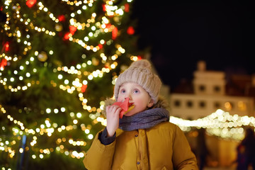 Wall Mural - Little boy is eating snack near large Christmas fir tree. Xmas holidays on famous fair in Tallinn, Estonia.