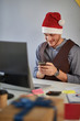 © luckybusiness - Business man in santa hat working at a computer at Christmas  at office.