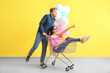 © Pixel-Shot - Young couple with shopping cart and balloons near color wall