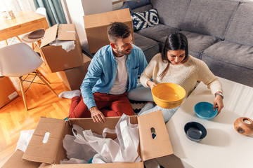 Wall Mural - Smiling young couple move into a new home sitting on floor and unpacking.