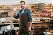 © LIGHTFIELD STUDIOS - cheerful carpenter in apron standing and holding wooden plank in workshop
