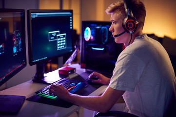 male teenage hacker sitting in front of computer screens bypassing cyber security