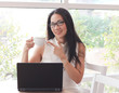 © Phuttharak - Beautiful Asian woman wearing eye glasses sitting by the window with computer laptop on table , pointing to cup of coffee