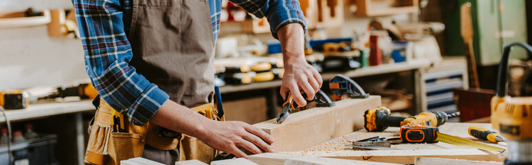 panoramic shot of carpenter holding pliers near wooden dowel