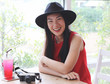 © Phuttharak - Beautiful Asian woman wearing black hat sitting by the window with camera and red drink  on table