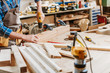 © LIGHTFIELD STUDIOS - cropped view of carpenter in apron holding hammer drill near wooden planks in workshop