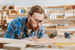 © LIGHTFIELD STUDIOS - selective focus of carpenter in goggles holding hammer drill and blowing on sawdust near wooden plank
