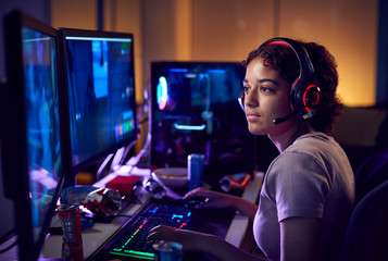 Teenage Girl Wearing Headset Gaming At Home Using Dual Computer Screens