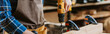 © LIGHTFIELD STUDIOS - panoramic shot of carpenter in apron holding hammer drill near wooden plank