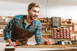 © LIGHTFIELD STUDIOS - selective focus of cheerful bearded woodworker holding pencil near measuring tape in workshop