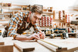 © LIGHTFIELD STUDIOS - Selective focus of handsome woodworker holding pencil while measuring wooden plank