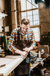 © LIGHTFIELD STUDIOS - selective focus of handsome woodworker holding chisel while carving wood in workshop