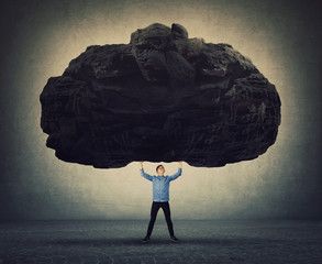 Brave man making effort facing life problems as holding a huge boulder about to squeeze him. Difficult task, guy convinced in his powers, standing up to troubles. Super strength, burden concept.