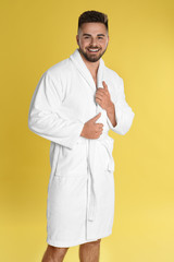 Happy young man in bathrobe on yellow background