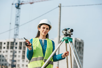 Smiling surveyor with digital level and radio set on construction site