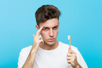 Wall Mural - Young caucasian man holding a toothbrush Young indian woman wearing a pajamas and sleep mask isolated holding a pillow pointing his temple with finger, thinking, focused on a task.< mixto >