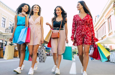 Wall Mural - Perfect weekends. Low-angled photo of four beautiful women in summer dresses, walking towards the camera in the city center with their purchases from the mall.