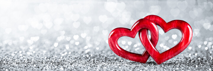 Wall Mural - banner of two red wooden interlocking hearts on silver glitter with heart shaped bokeh background - 