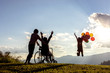 Happy family on the mountain,woman is on a wheelchair looking little girl jumping playing with air balloons at sunset.