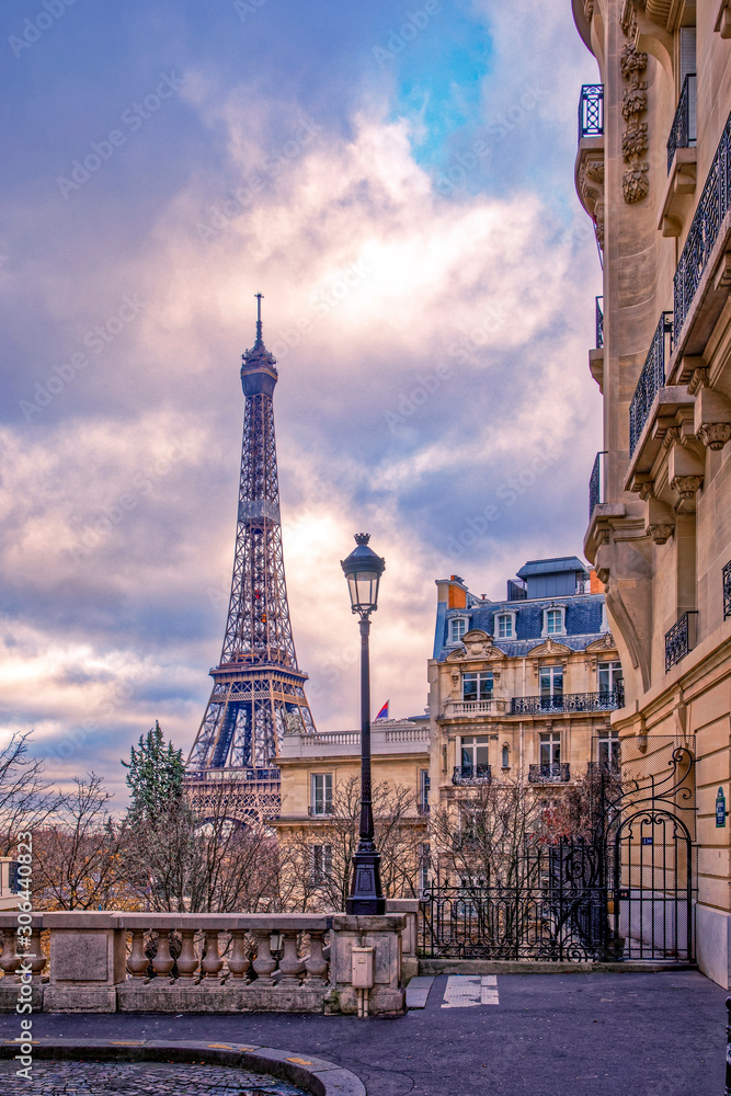 Paris, France - November 24, 2019: Small paris street with view on the famous paris eiffel tower on a cloudy day with some sunshine - obrazy, fototapety, plakaty 