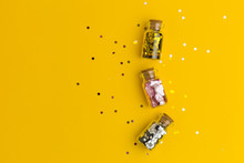 New Year And Christmas Yellow Background. Holidays,shopping And Sales Concept. Three Small Glass Bottles With Confetti, Top Horizontal View.