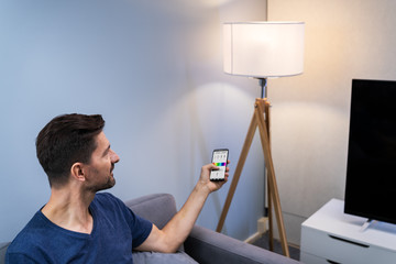 Wall Mural - Human Hand Adjusting Electric Light Through Mobile Phone