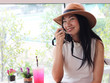 © Phuttharak - Beautiful Asian tourist woman wearing  hat  sitting in coffee shop with red drink on table holding her camera