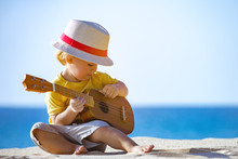 Kid Plays On Ukulele Or Small Guitar At Sea Beach